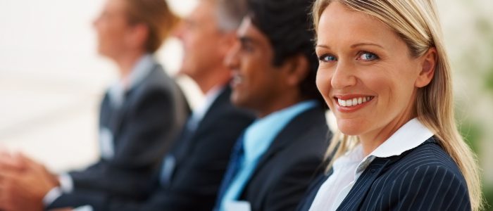 row of people sitting at a meeting with focus on woman smiling at the camera