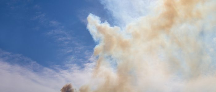 Smoke billowing in the air from a wildfire in Colorado with the sun shining through the smoke.