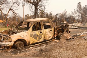 Charred truck in front of home burned to the ground in the recent wild fire fire storm in Redding, California. Smoke and ash in the air as the fire continues to burn several miles away.